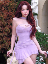 Woman in a lavender dress standing outdoors with greenery and a statue in the background